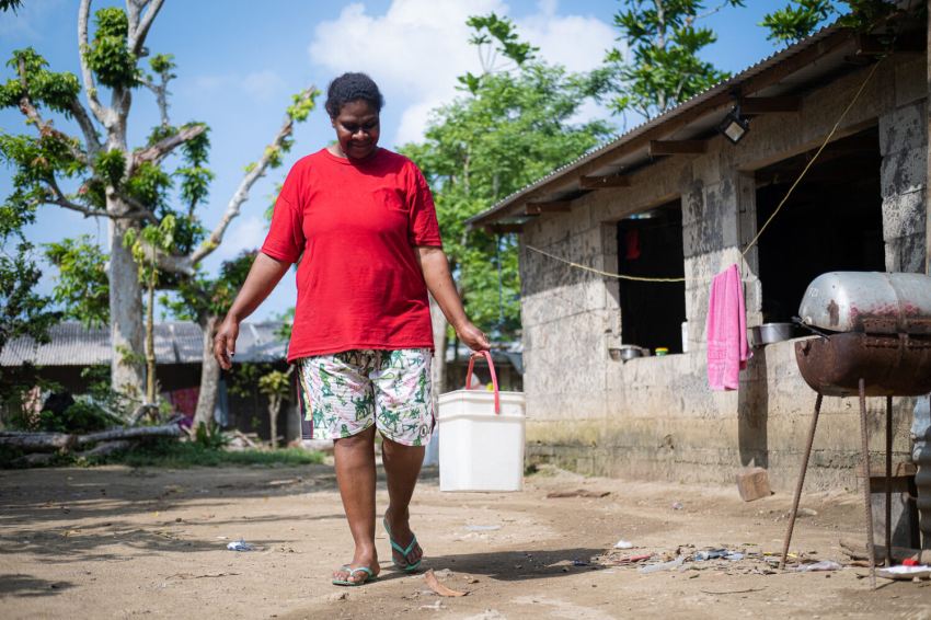 person walks through village with bucket of water