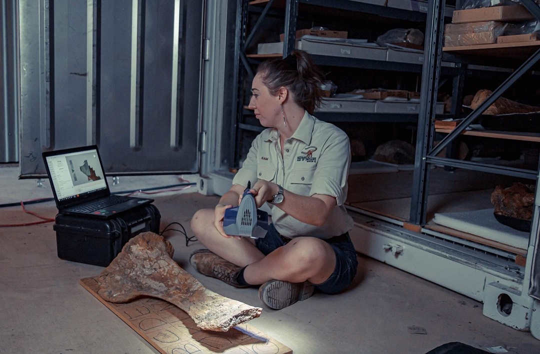 palaeontologist sitting on the ground scanning a fossil bone