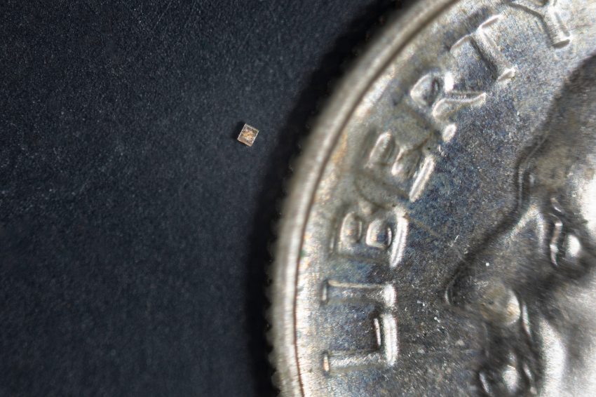 Photograph of a tiny sensor, the size of a grain of salt, next to a coin for scale