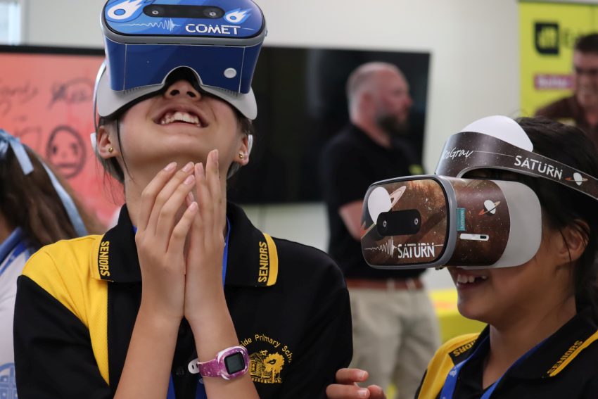 Two young girls wearing VR goggles, one with Saturn and the  other Comets printed on the headpiece.