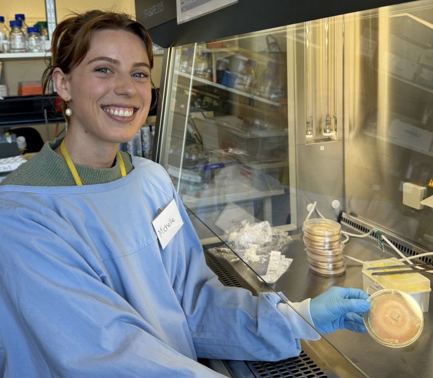 Photograph of a young woman in a lab, holding a petri dish with fungus growing on it