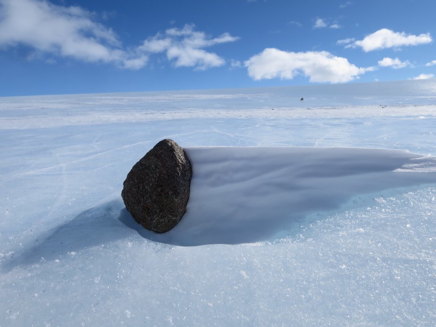 Photograph of a black meteorite on a frozen landscape