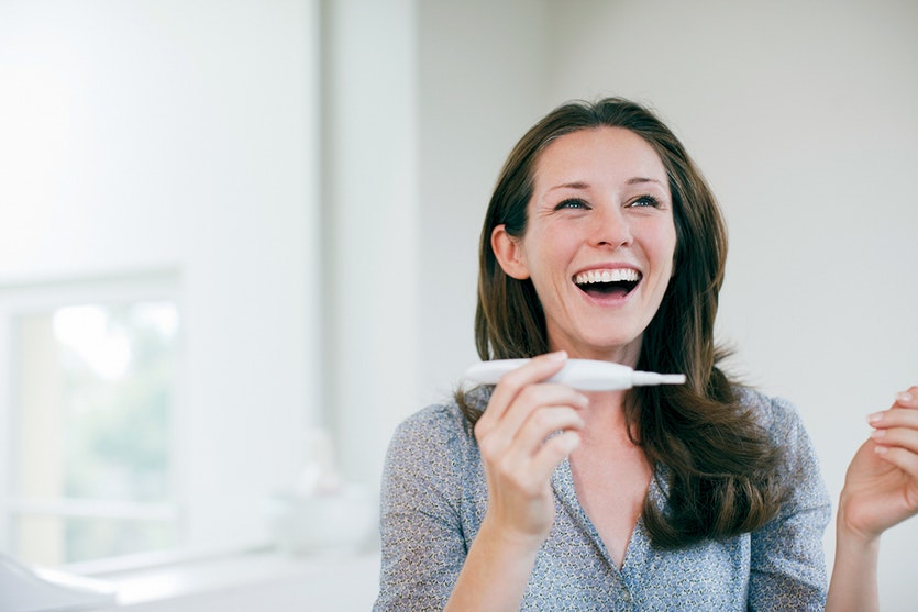 A woman holding a pregnancy test and looking happy.