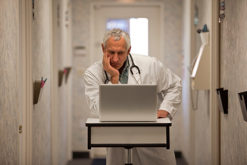 A perplexed doctor stares a computer.