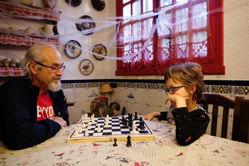 An old man playing chess with a young boy.