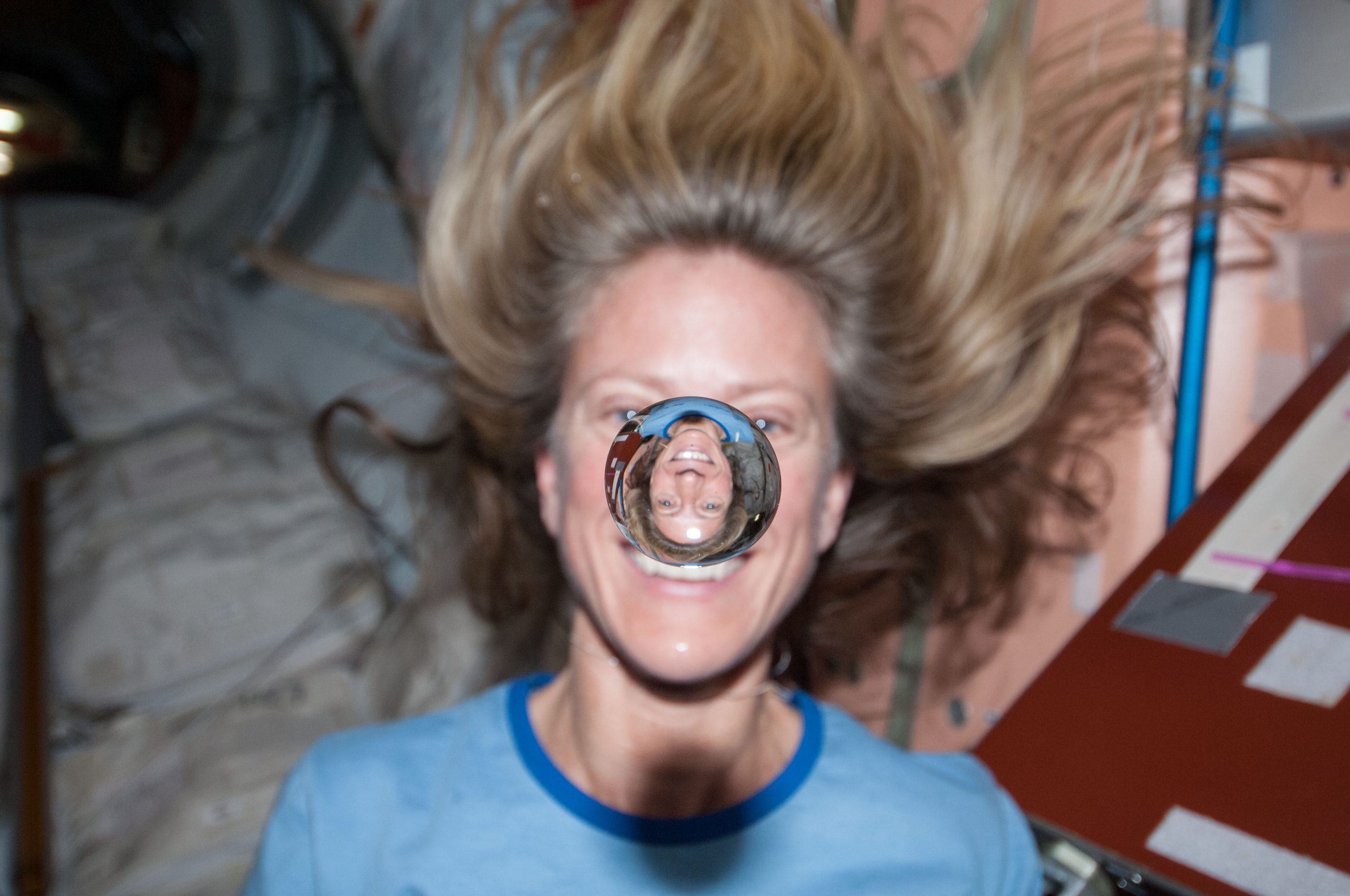 Astronaut karen nyberg watches a water bubble float freely between her and the camera, showing her image refracted in the droplet.