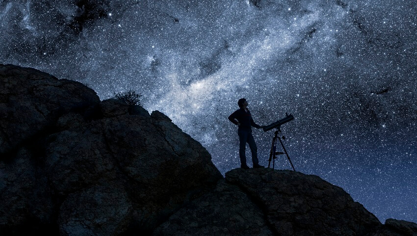 man looking at stars next to telescope