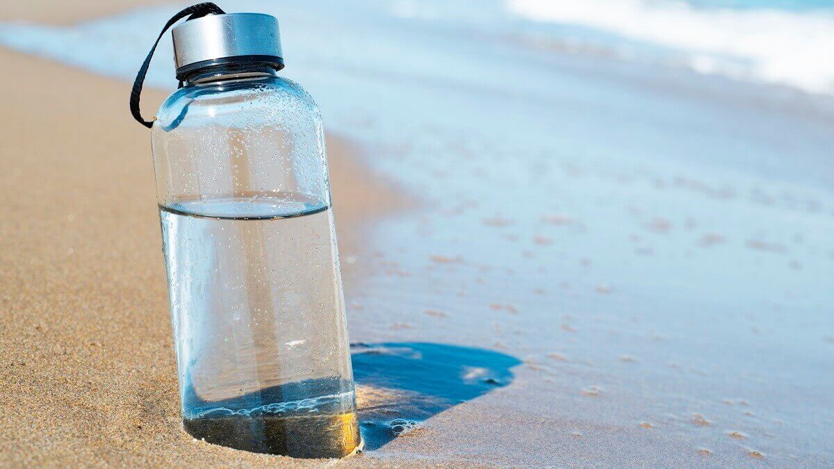 A water bottle filled with fresh water next to the ocean. New research may improve desalination techniques.