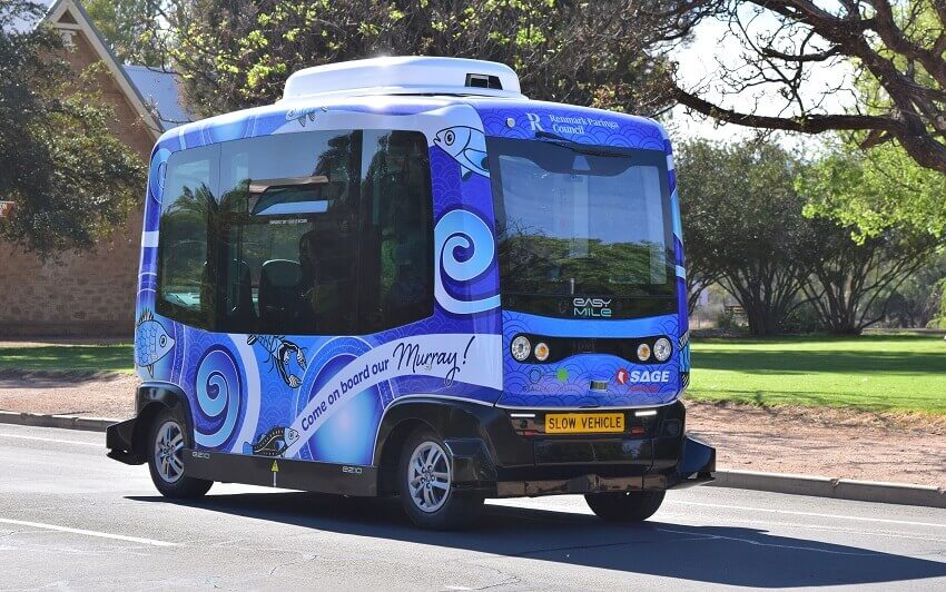 A small blue bus drives along a road. This is murray, the driverless bus being trialled in renmark, south australia.