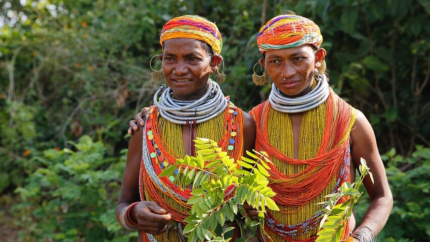 Indigenous villagers in the heavily forested state of Odisha, India, dressed in orange, white and red, and holding leaves.