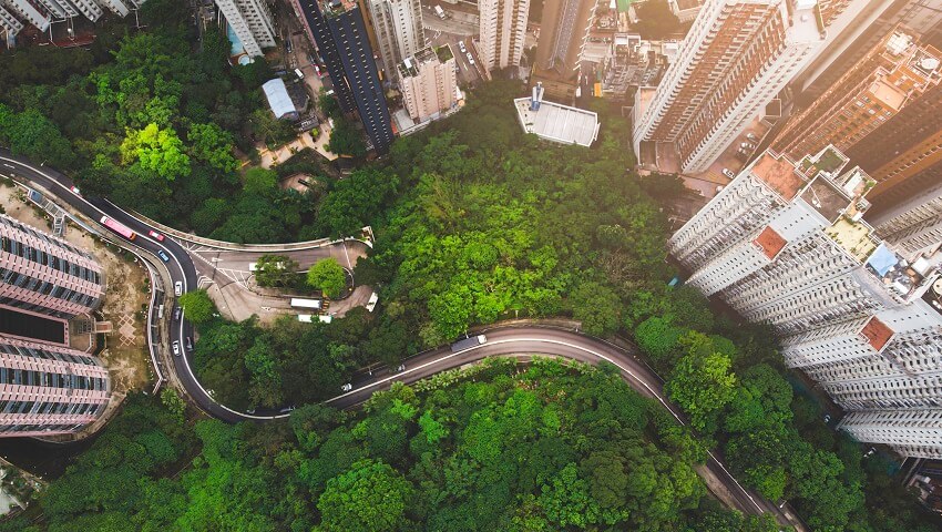 Aerial view of building in honk kong next to a forest. There is a road in the trees.