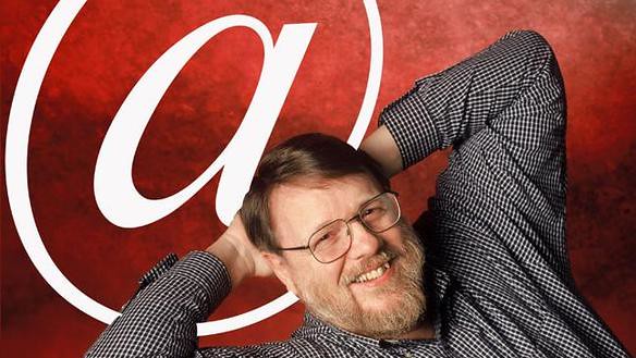 A man witha beard lies on a red background with a large white asperand. The man wears glasses and a grey shirt. He is smiling and his hands are behind his head