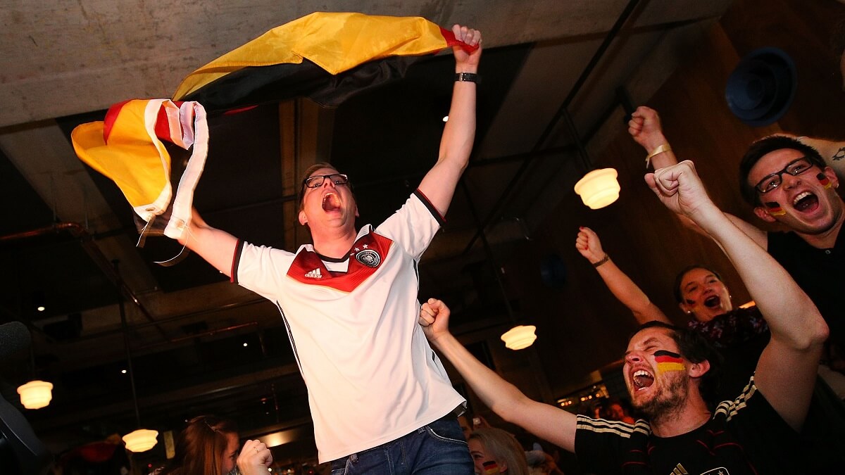 A man in a football shirt waves a german flag. He seems to be yelling