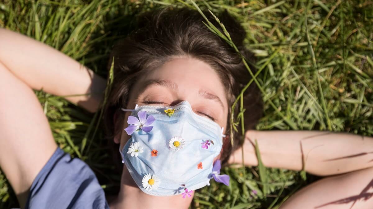 Woman lies sleeping in a field, wearing a mask that's been decorated with flowers