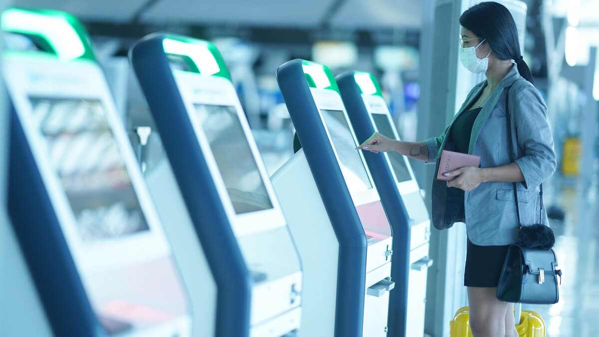Woman wearing a mask uses a public touch screen to check in at an airport