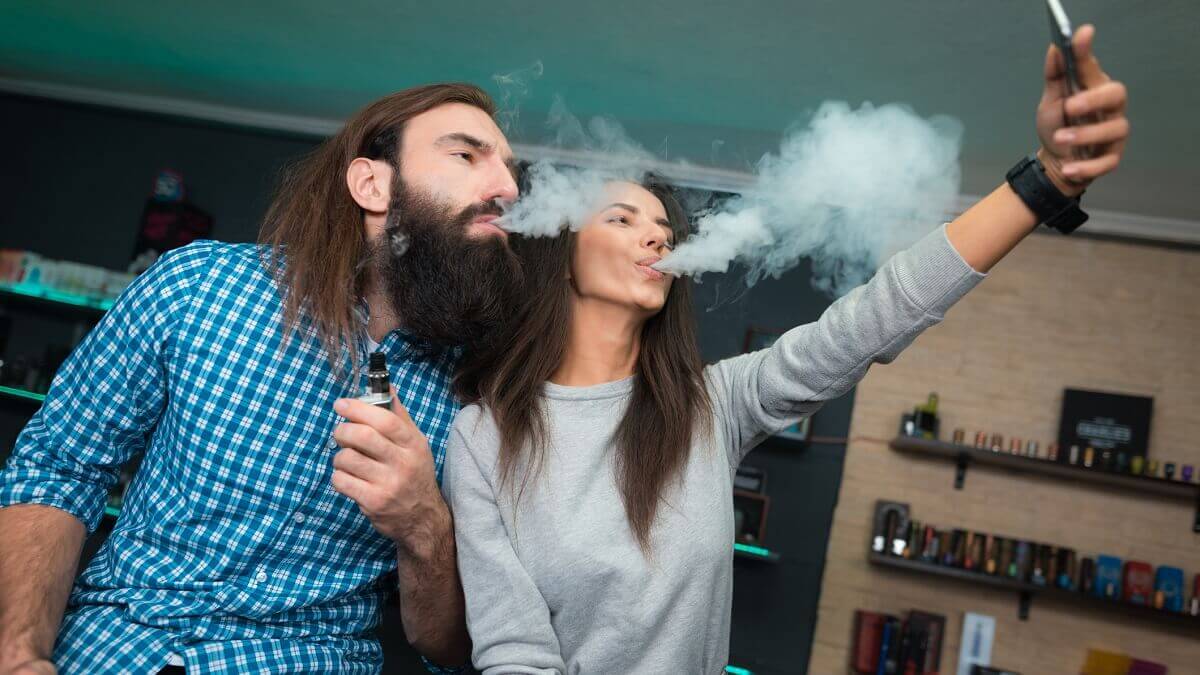 A man and a woman taking a selfie together while vaping in a vape shop.