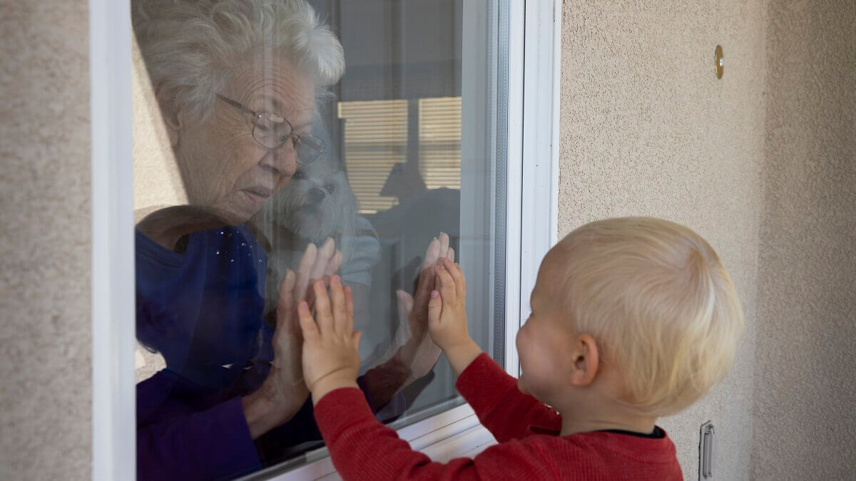 Elderly woman greets her infant grandchild through a glass window.