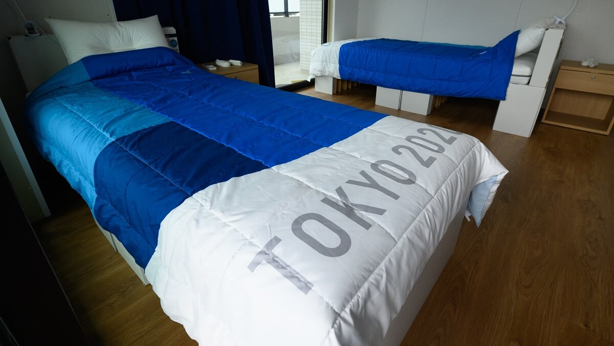 Two beds with white and blue bedspreads. The closest bed says tokyo 2020