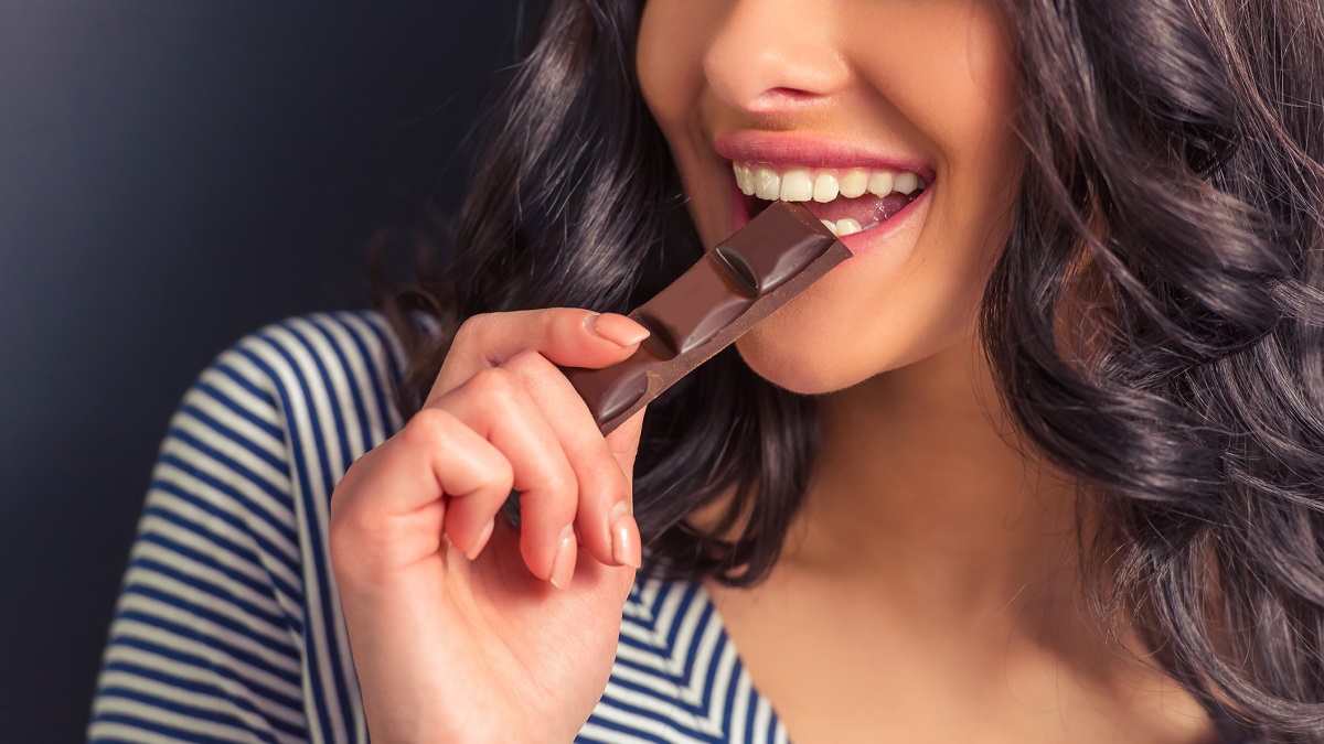 Cropped image of a girl eating chocolate and smiling, against dark background