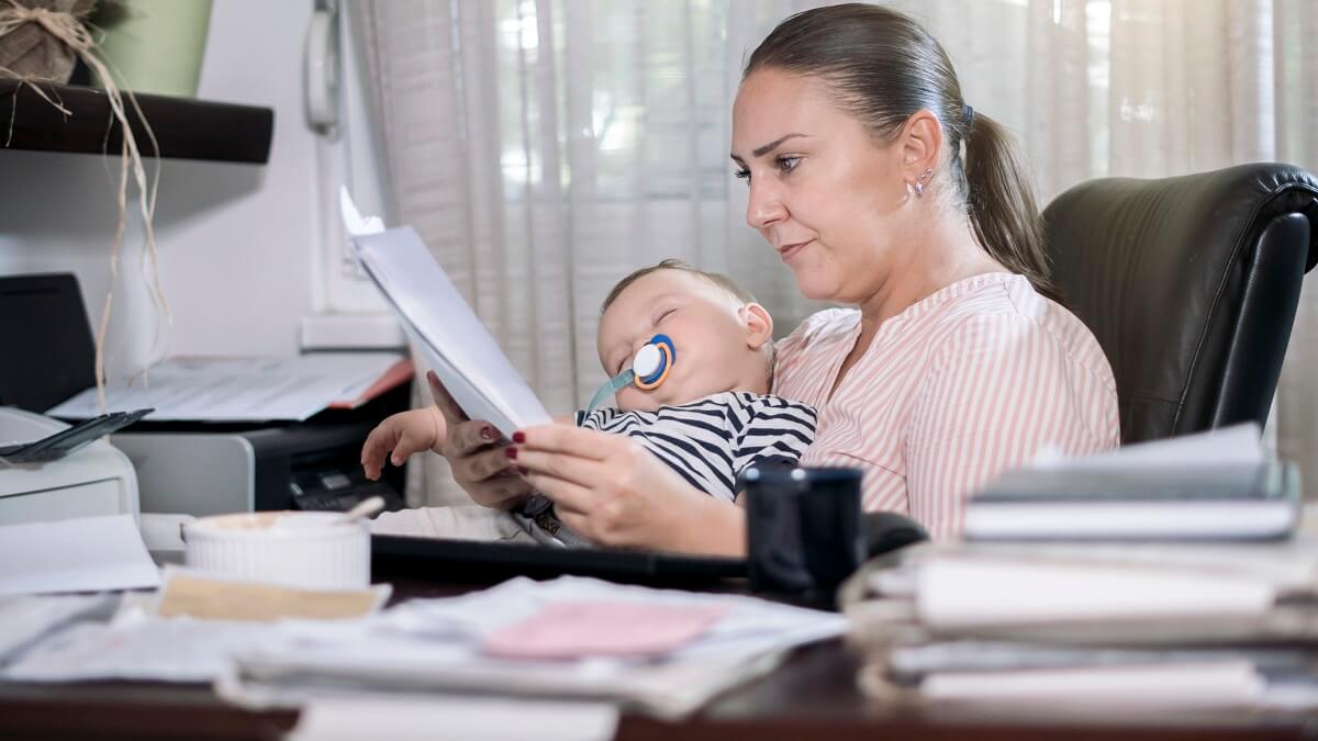 Photo of a mother working from home while holding a sleeping baby