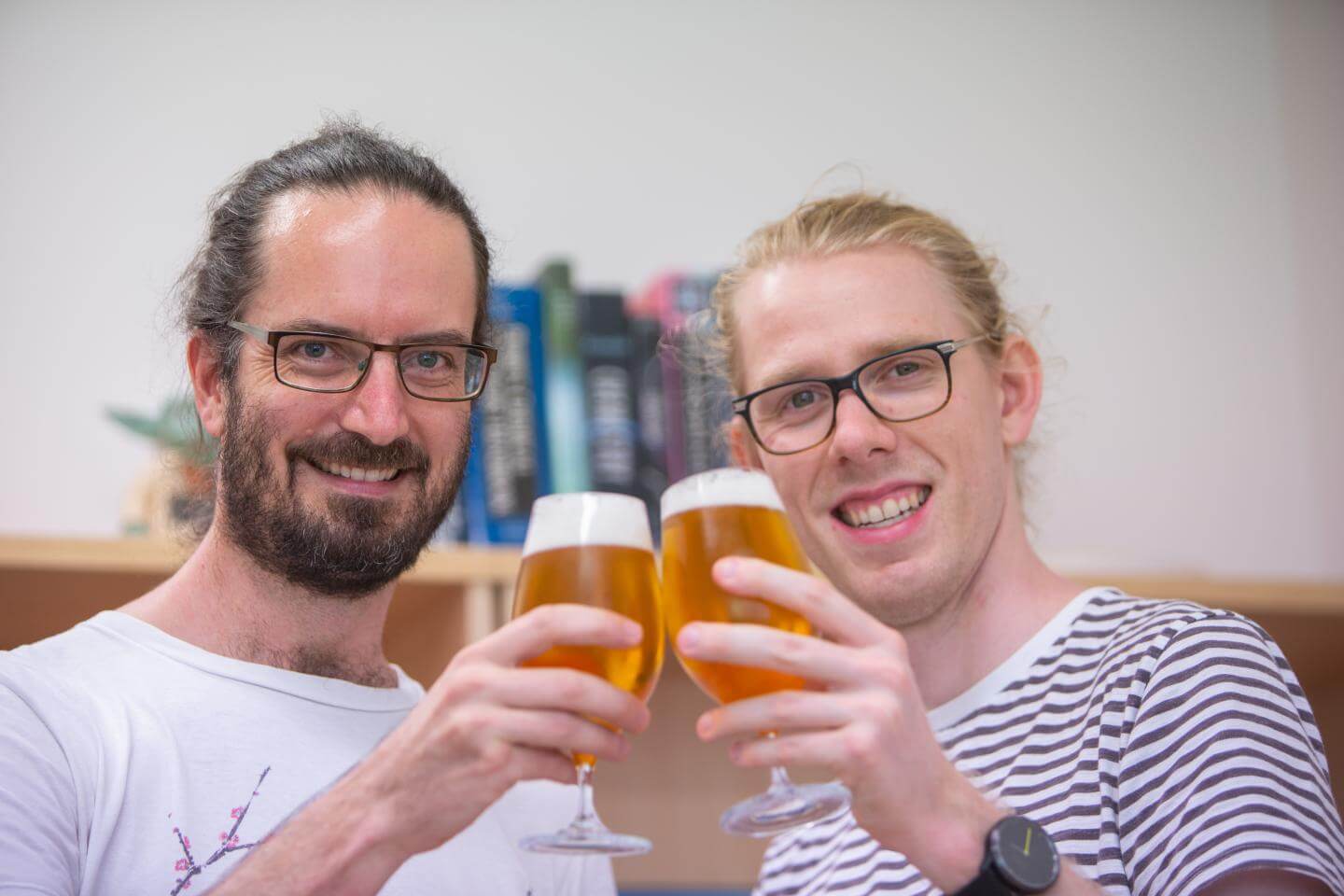 Two men hold up glasses of beer.