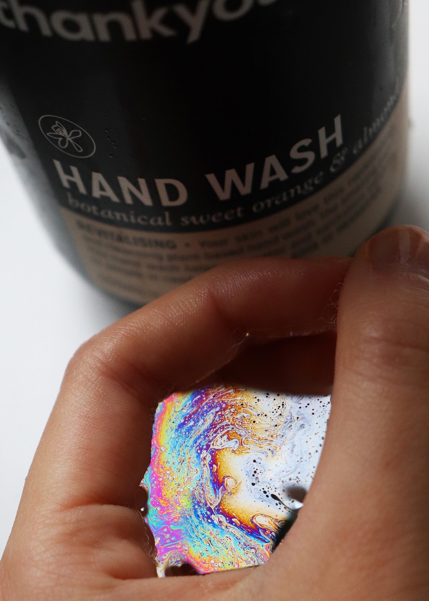 Hand next to a bottle labelled 'hand wash', hand is holding a soap bubble