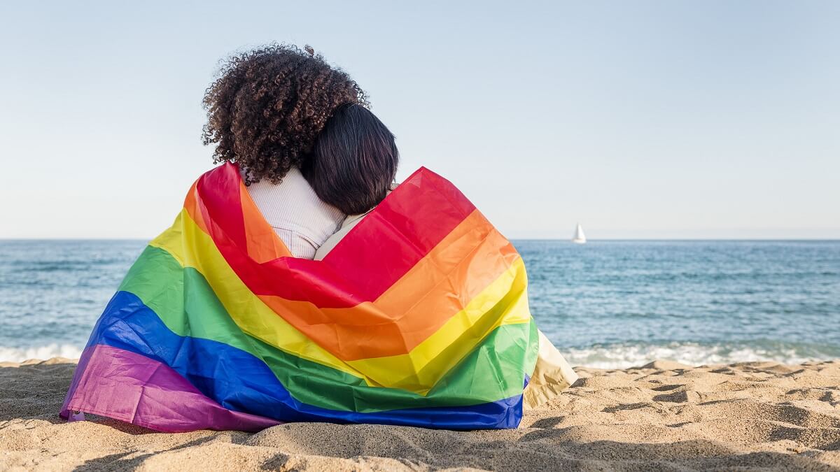 two women sitting on a beach wrapped in a rainbow flag