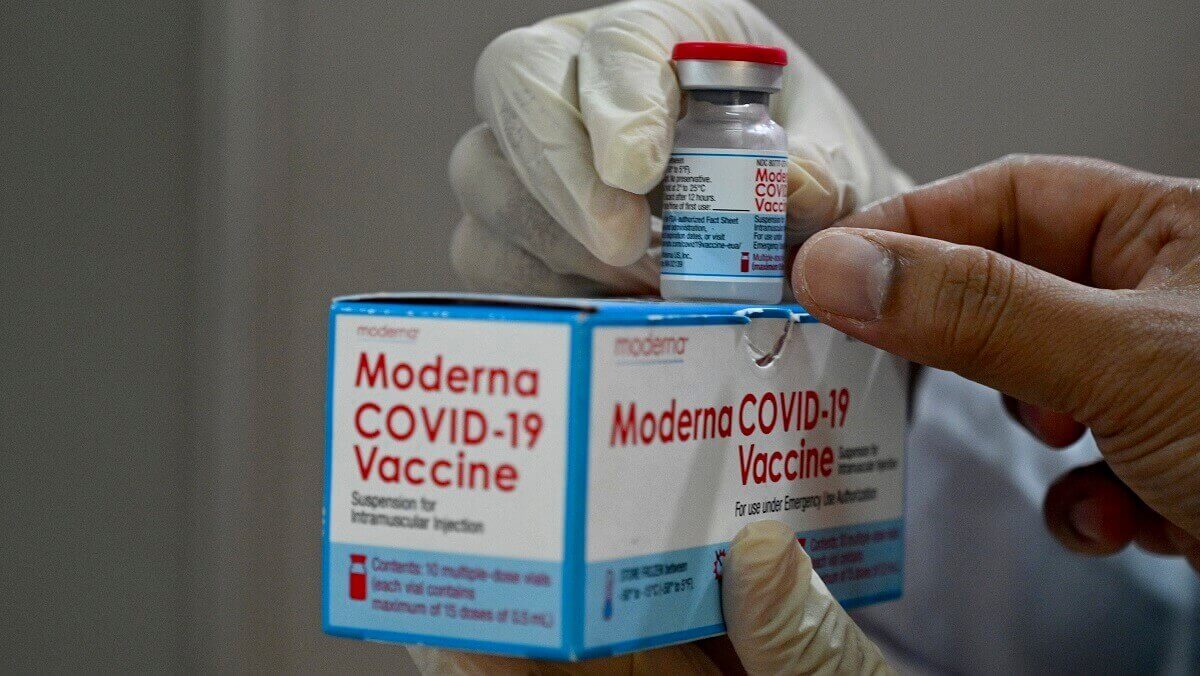 a mox that says MODERNA COVID-19 vaccine and a bottle on top. It is being held by gloved hands