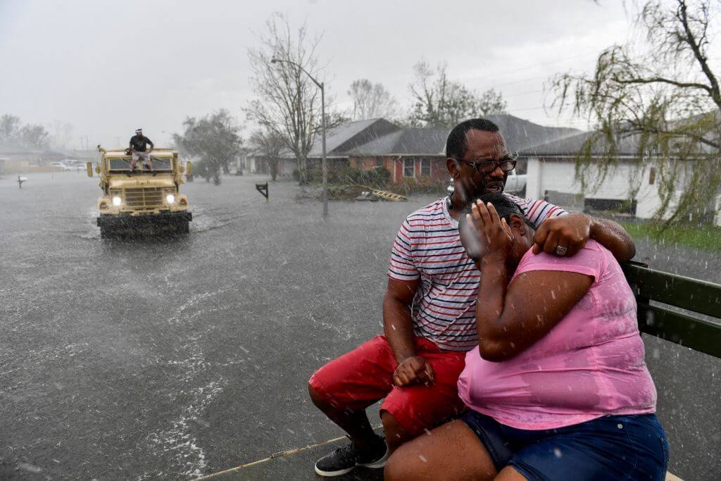 A man holding a crying woman in a flooded street as rain pours down