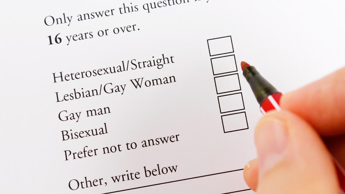 A questionare that askes about sexuality. some fingers with a red pen in hand is hovering above it