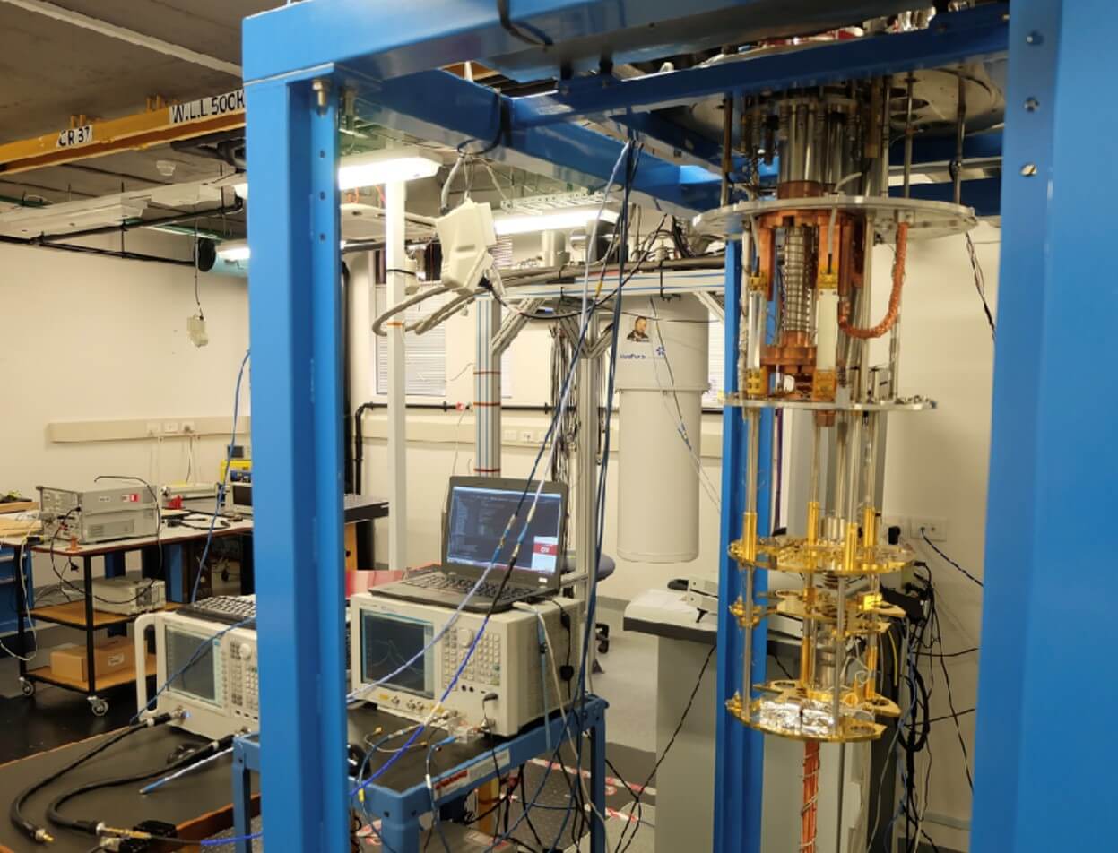 A lab set up with computers, signal processing units, and a cryogenic cylinder