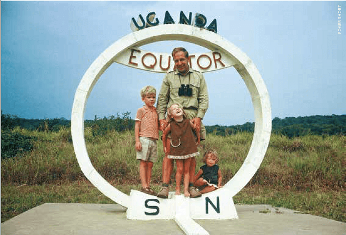 A man and three young children stand at a monument marking the equator in uganda.