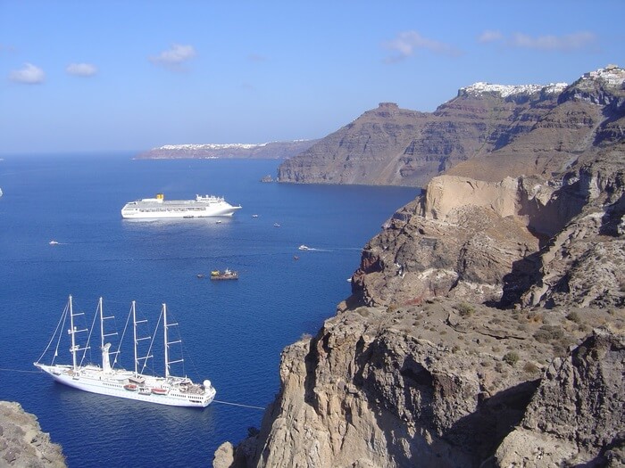 Photo of boats beside santorini's cliffs, showing layers deposited by past eruptions