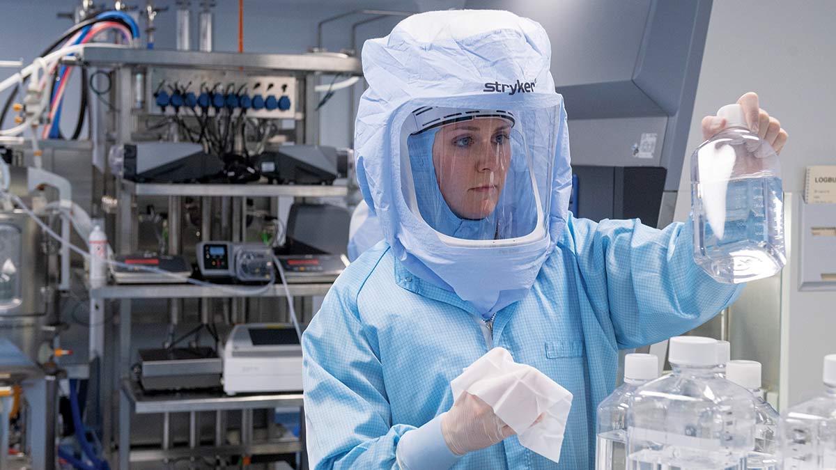 woman in a covred suit examines bottles in an mrna vaccine laboratory