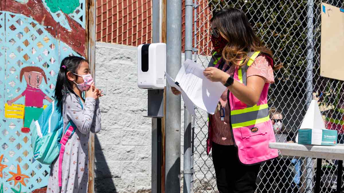young girl and woman wearing masks stand outside a school