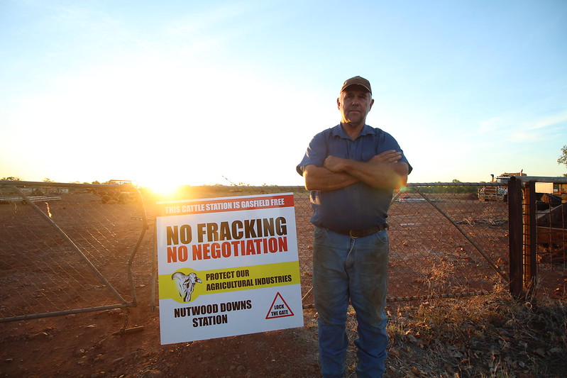 Man standing in front of a gate with a sign saying "no fracking, no negotiation"