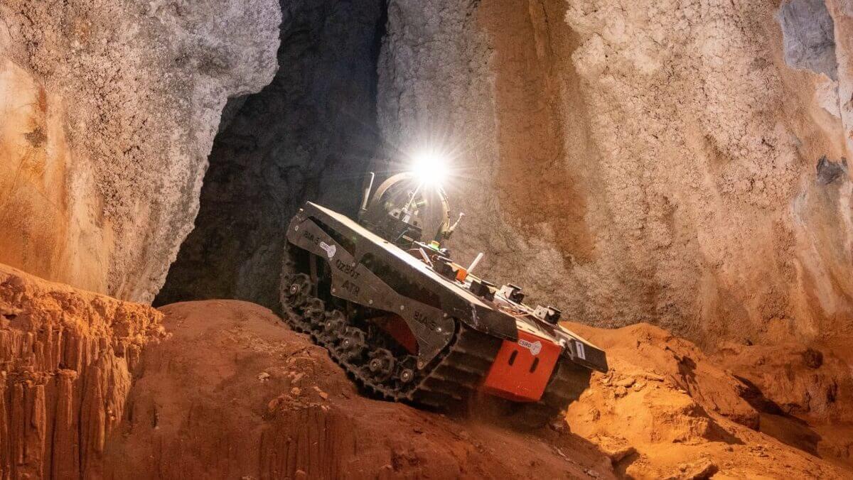 a robot with tracks. It has a light on top of it. It is in a cave
