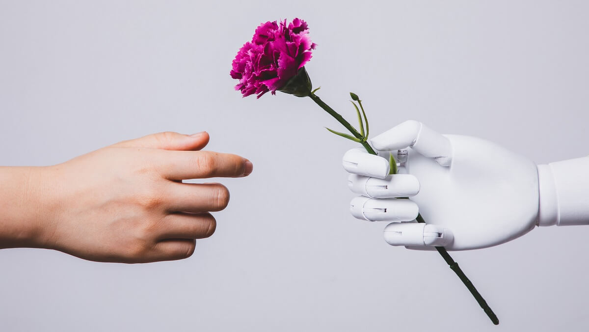 a robot hand holding a flower. A human hand reaches for it