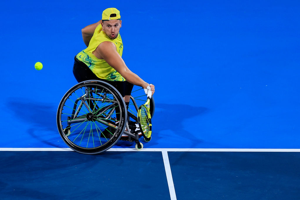 Man in wheelchair hits tennis ball with a racket.