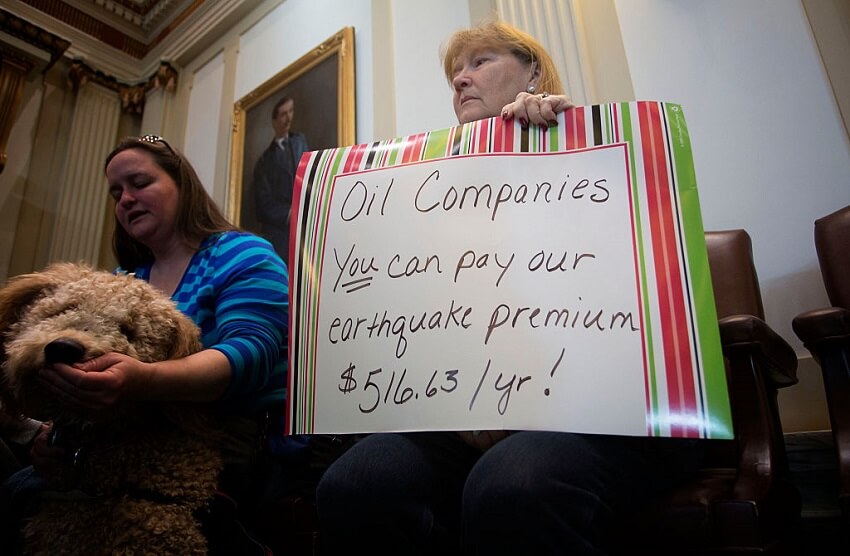 A women holds a sign reading "oil companies you can pay our earthquake premium of $516. 63/yr! "