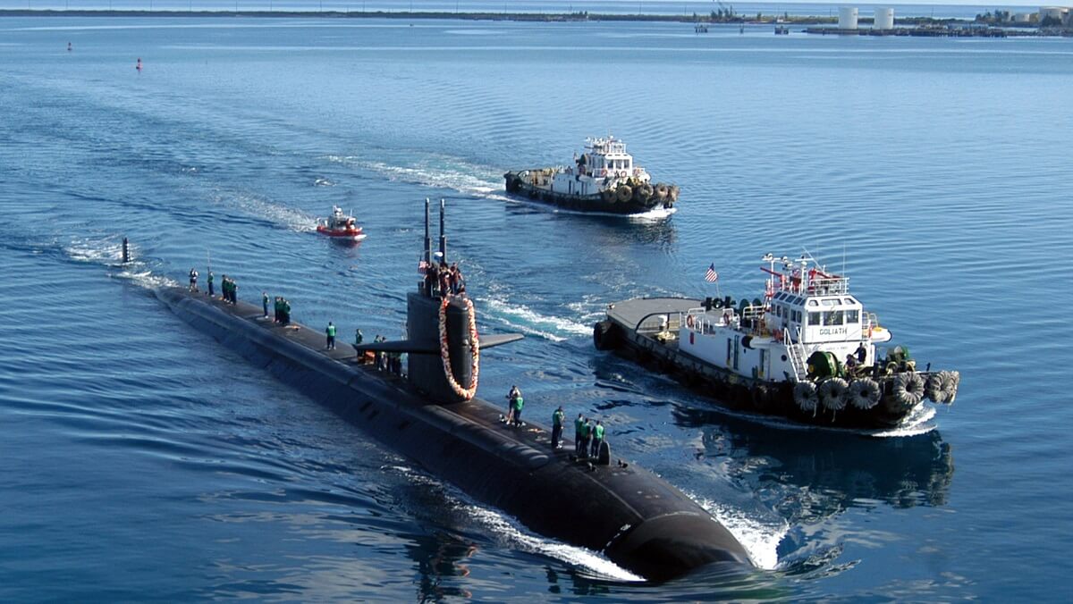 a submarine half in the water.There are two large ships next to it aand a small boat behind