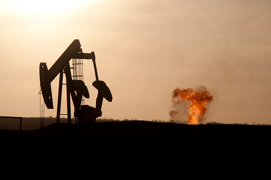 An oil well jack pump and natural gas flare off at sunset