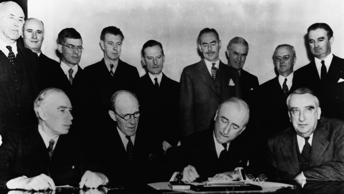 Lots of men wearing suirts standing together behind a desk. One person signs a document
