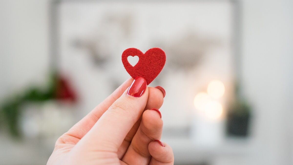A hand with painted red nails holding a small felt red heart