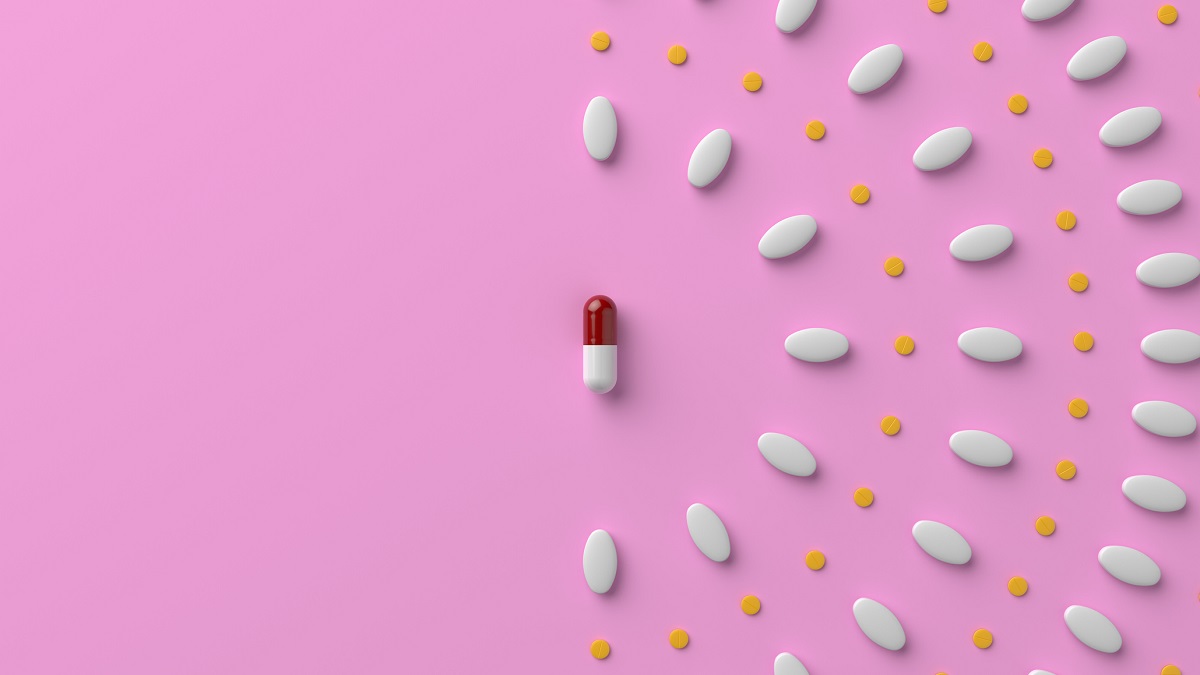 photo of pills of various size arranged in a pattern on a pink tabletop