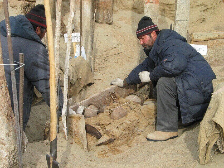 Two men in heavy jackets excavate a grave