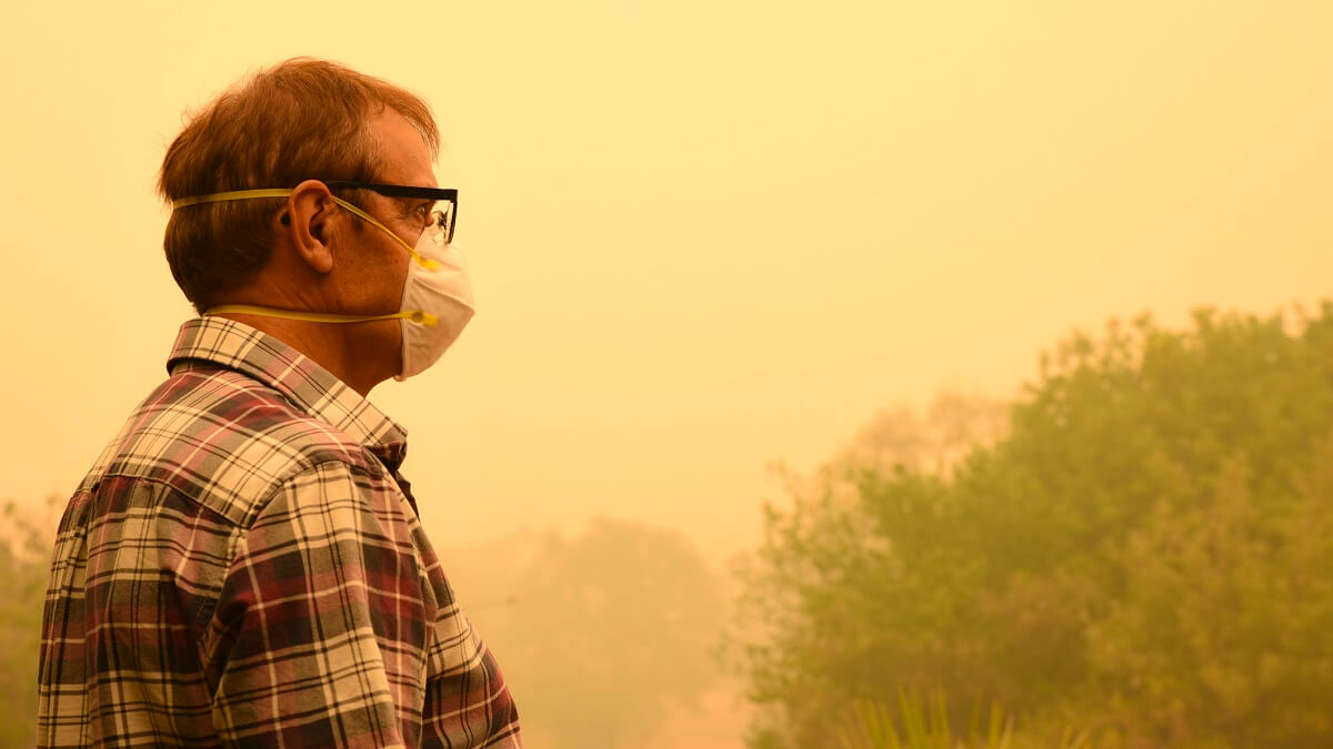 A man wears a face mask to protect himself against dangerous level of air pollution. He is standing in thick yellow smoke haze