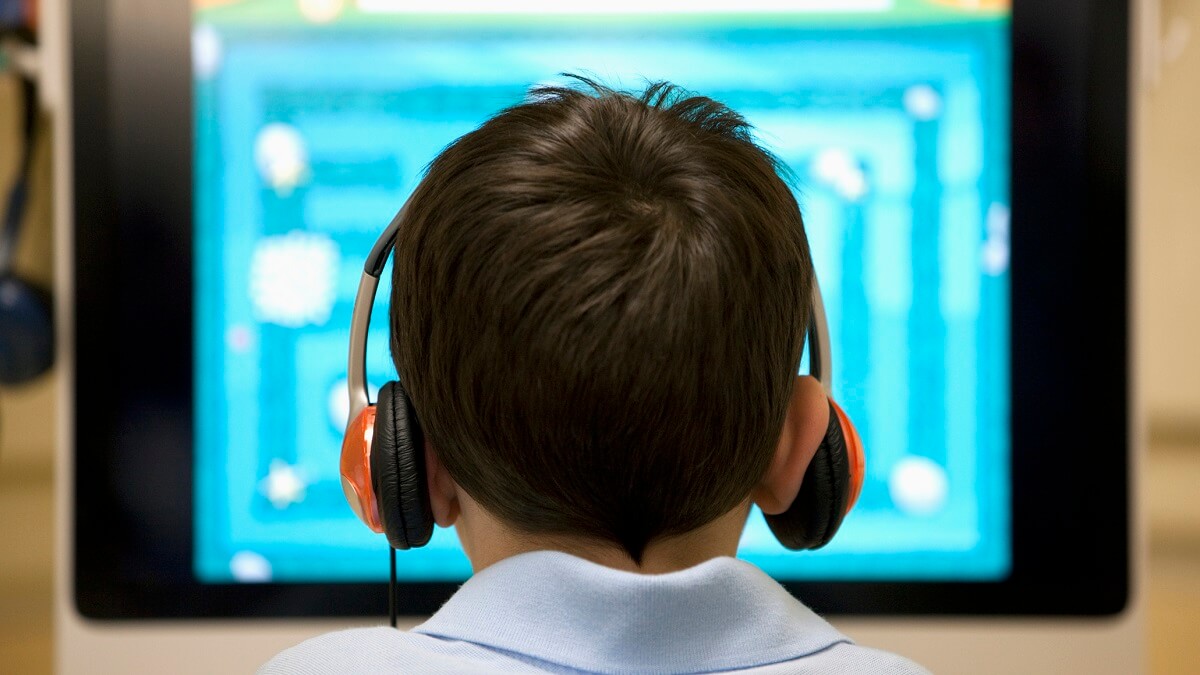 Rear view of a six year old boy at a computer workstation.