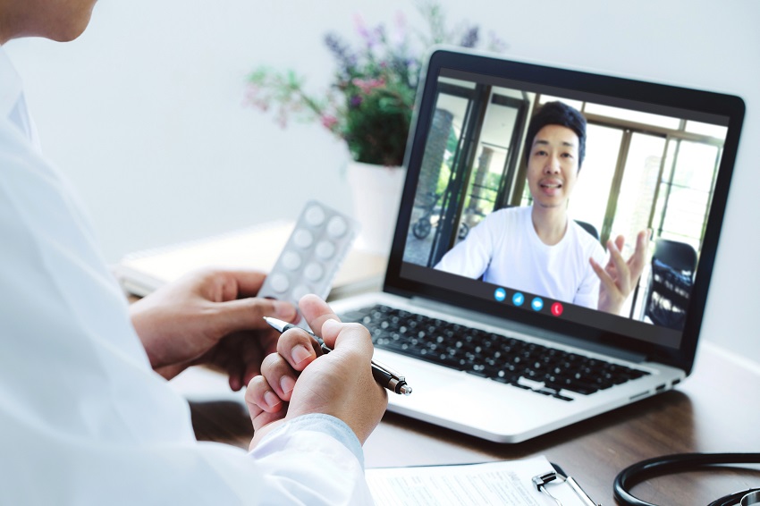 Doctor making video call and prescribing pills to man on computer screen.
