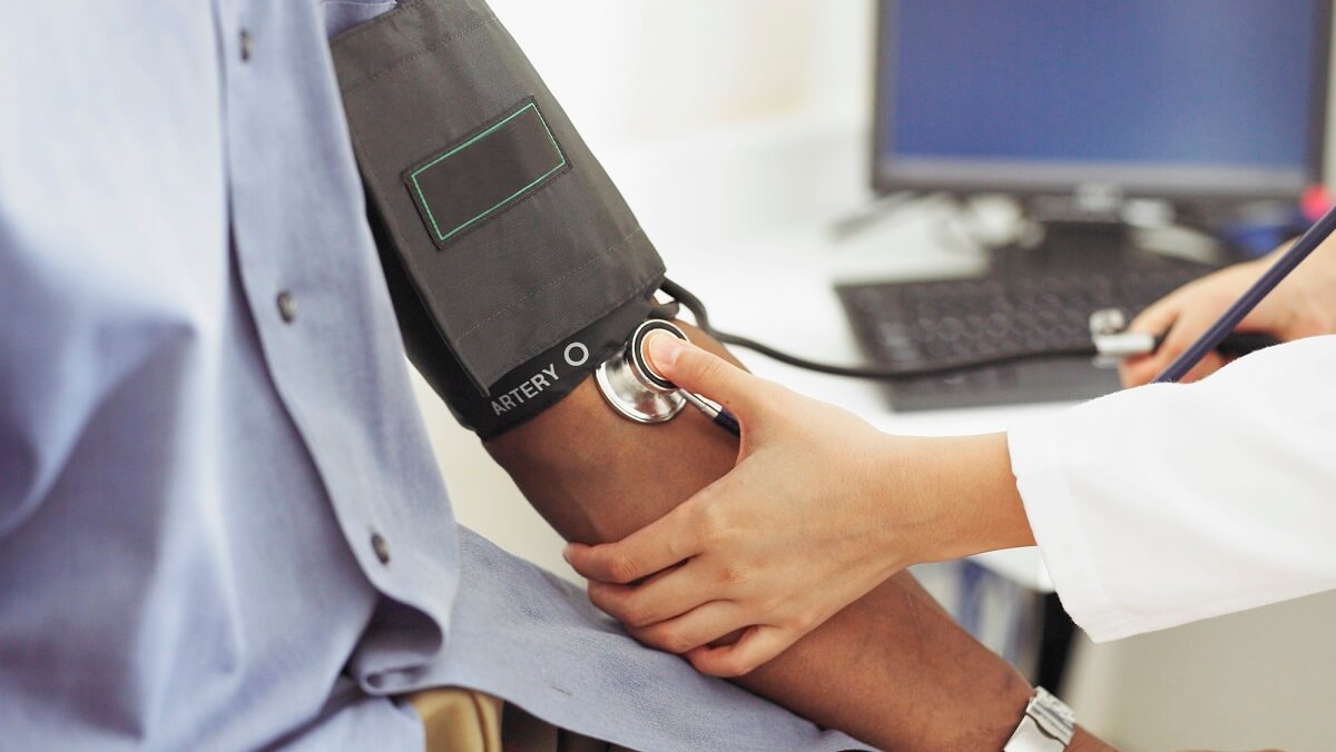 a person sitting with a blood pressure measurer around their arp. A doctor holds the pump